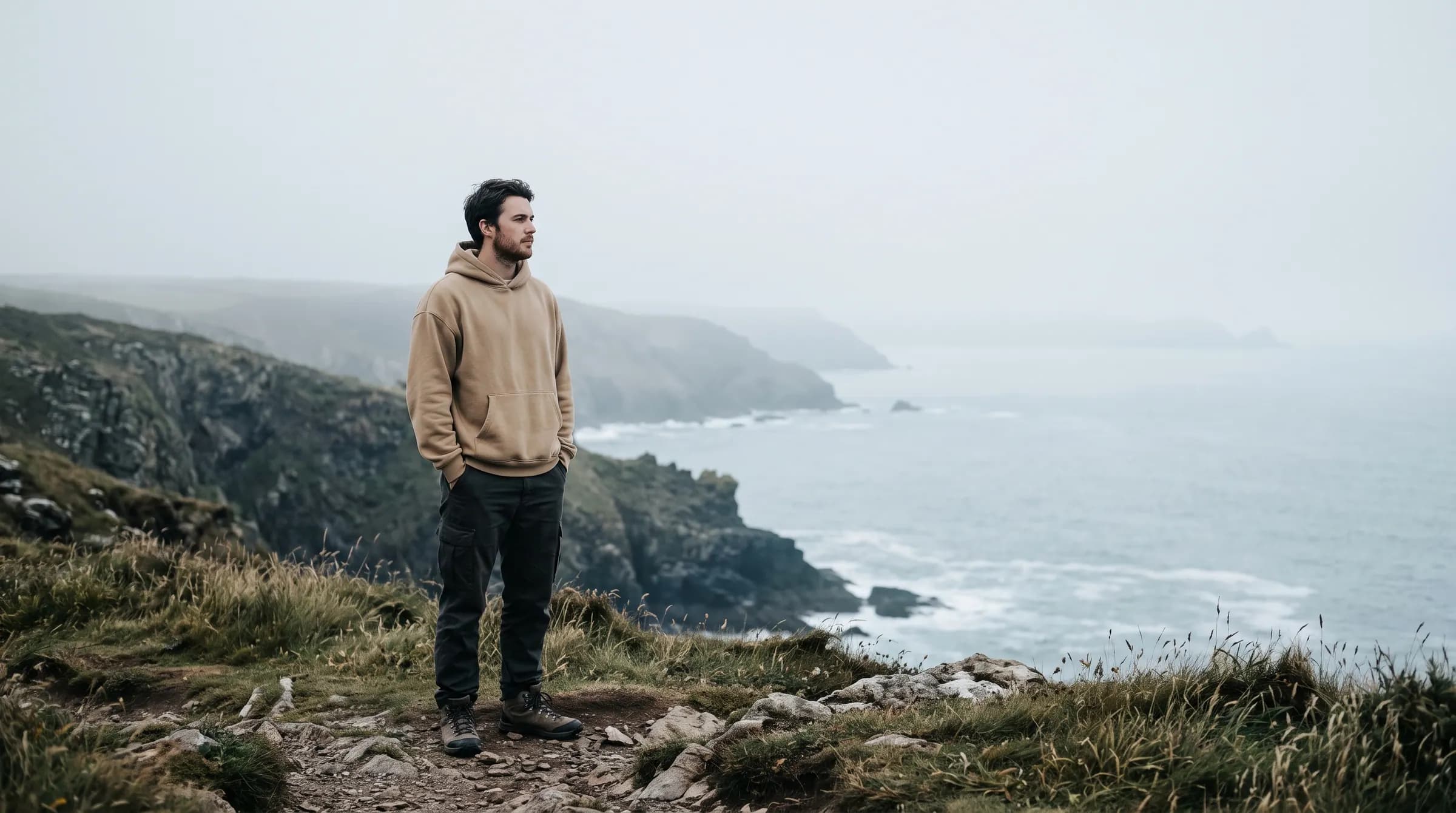 A man in a sand hoodie on a foggy coastal bluff